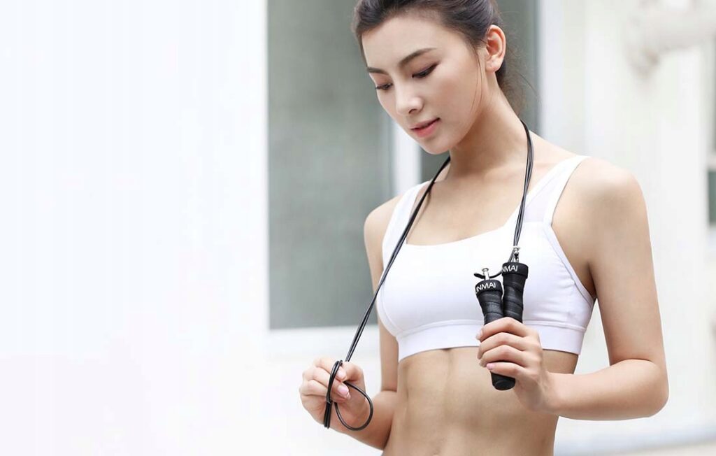 Czarna skakanka fitness Yunmai YMHR-P702 z akcesoriami w zestawieniu na gładkim tle